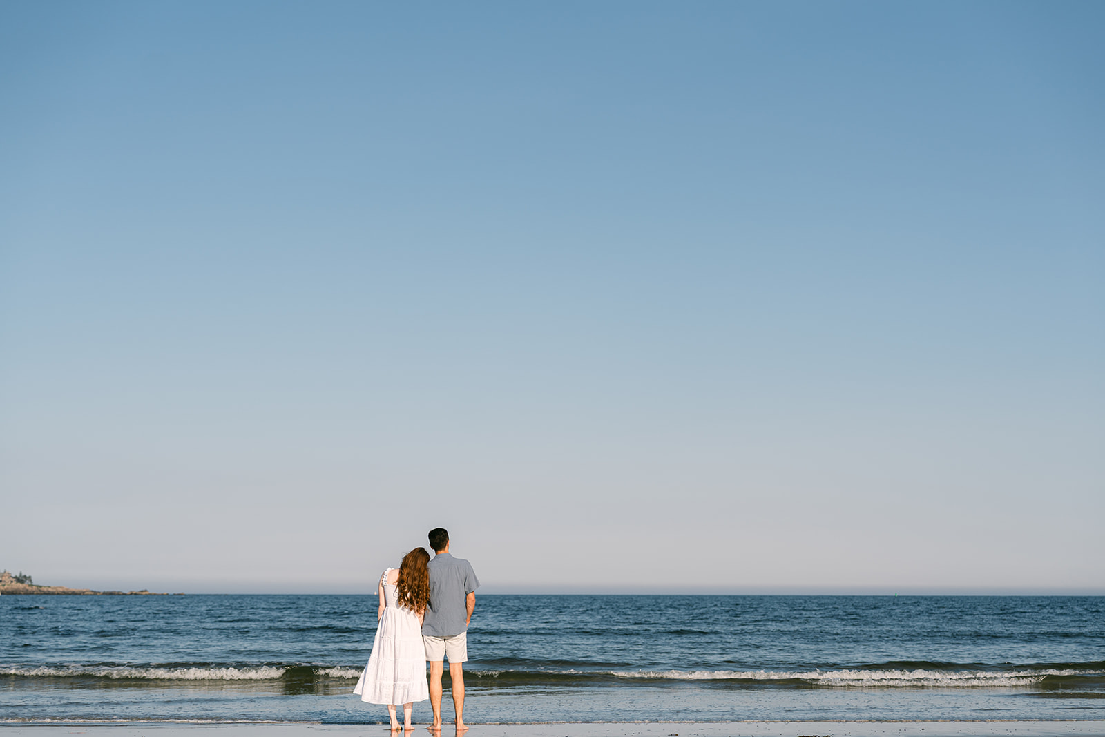 a couple staring our atthe ocean on a beach in Maine